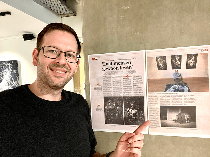Portrait of Dutch fine art photographer Arjan Spannenburg for his about page, pointing to a newspaper article about him and his work during an exhibition..