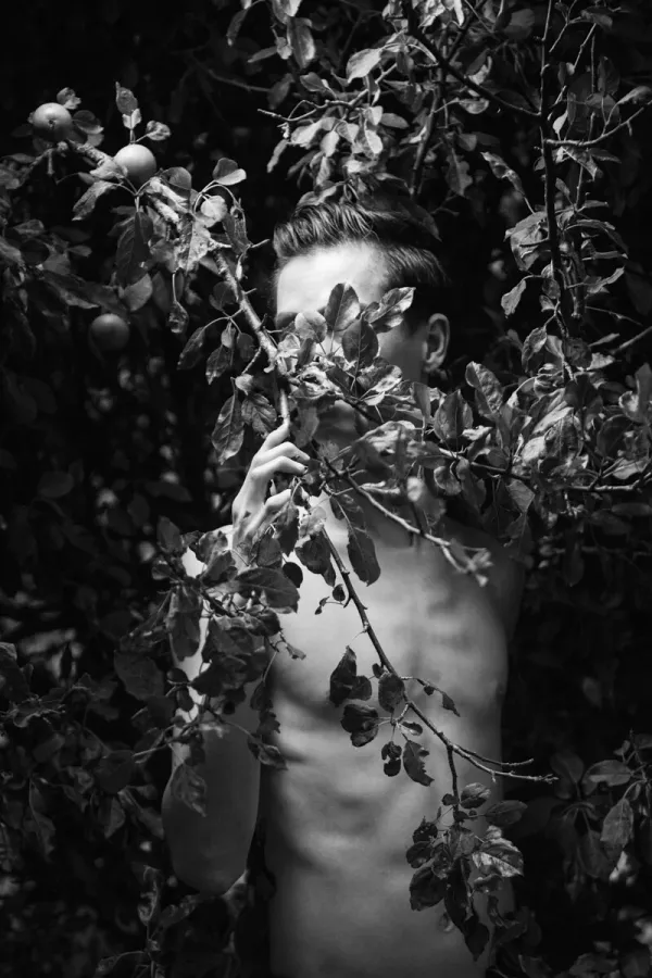 A black and white conceptual fine art portrait of BRANDON for the ESTRANGED series by ARJAN SPANNENBURG, featuring a man among apple tree branches.