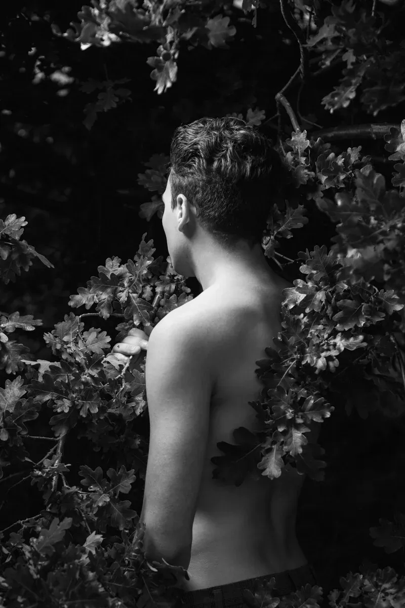 A black and white conceptual fine art portrait of CHRISTIAN for the ESTRANGED series by ARJAN SPANNENBURG, showing a man from behind among oak leaves.