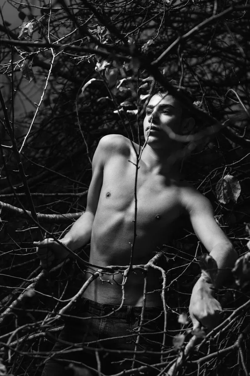 A black and white conceptual fine art portrait of DAMIAN for the ESTRANGED series by ARJAN SPANNENBURG, featuring a man among bare, leafless branches.