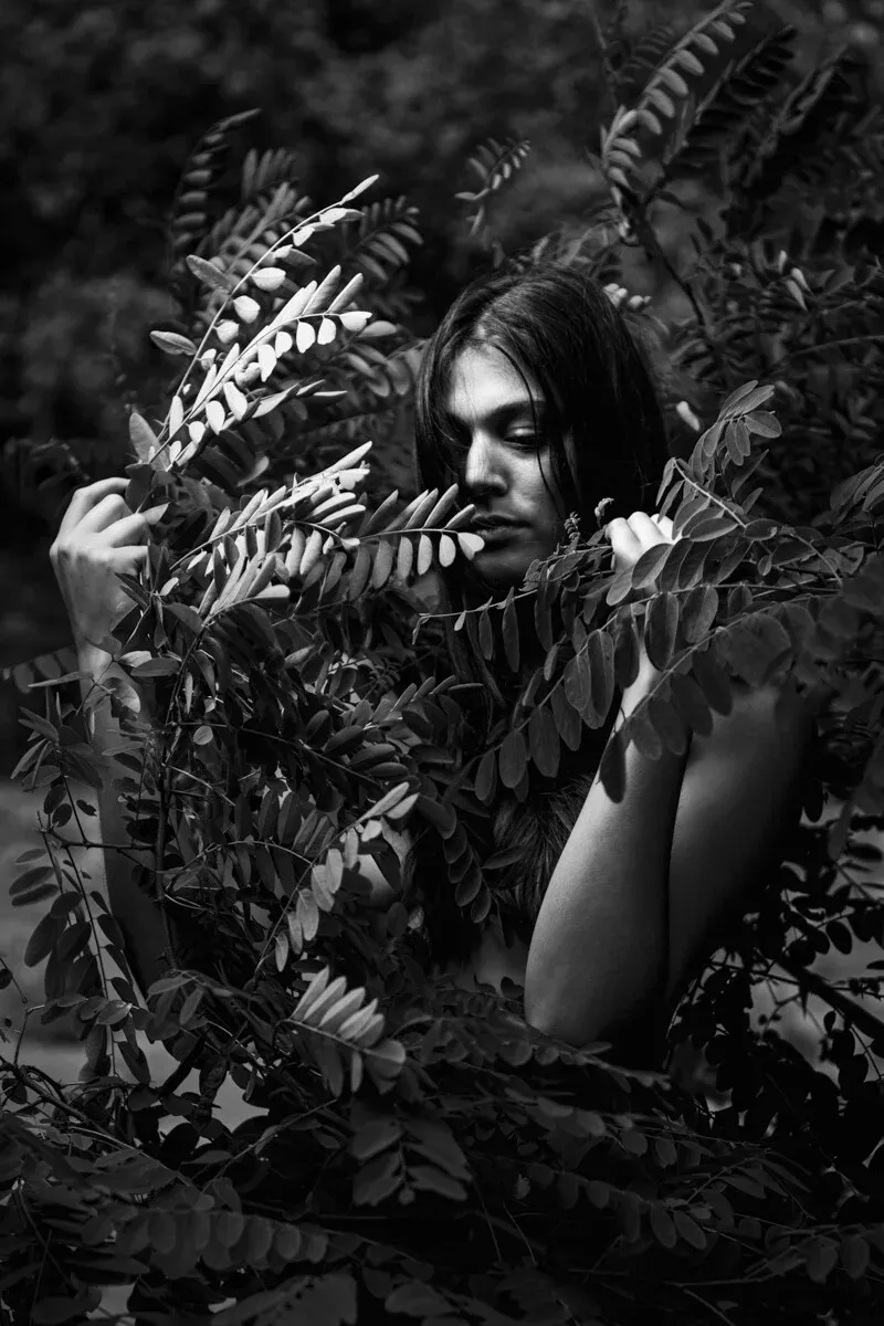 High-contrast monochrome photography of a person with long hair partially hidden by textured locust tree leaves, exploring themes of faith and self-recognition in ARJAN SPANNENBURG'S ESTRANGED series.