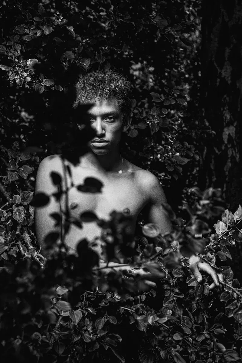 A black and white conceptual fine art portrait of JOEL for the ESTRANGED series by ARJAN SPANNENBURG, showing a man surrounded by dense leaves.