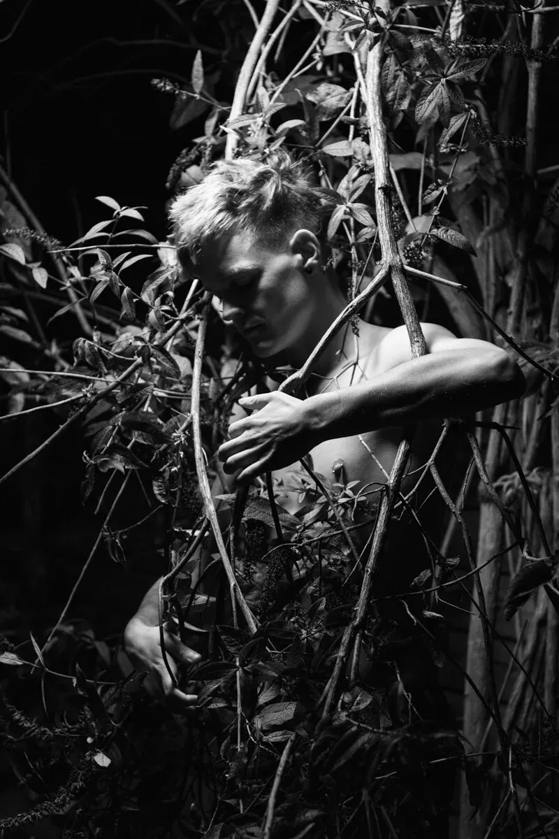 A black and white conceptual fine art portrait of SANDER for the ESTRANGED series by ARJAN SPANNENBURG, featuring a man among butterfly bush branches.