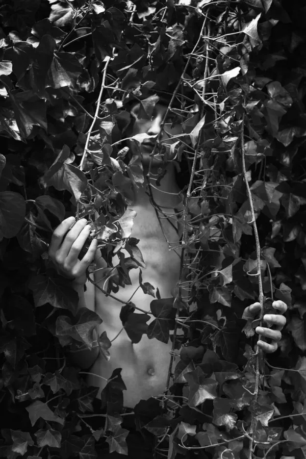 High-contrast monochrome photography of a young man partially hidden by ivy leaves, capturing the theme of self-worth and independence in ARJAN SPANNENBURG'S ESTRANGED series.