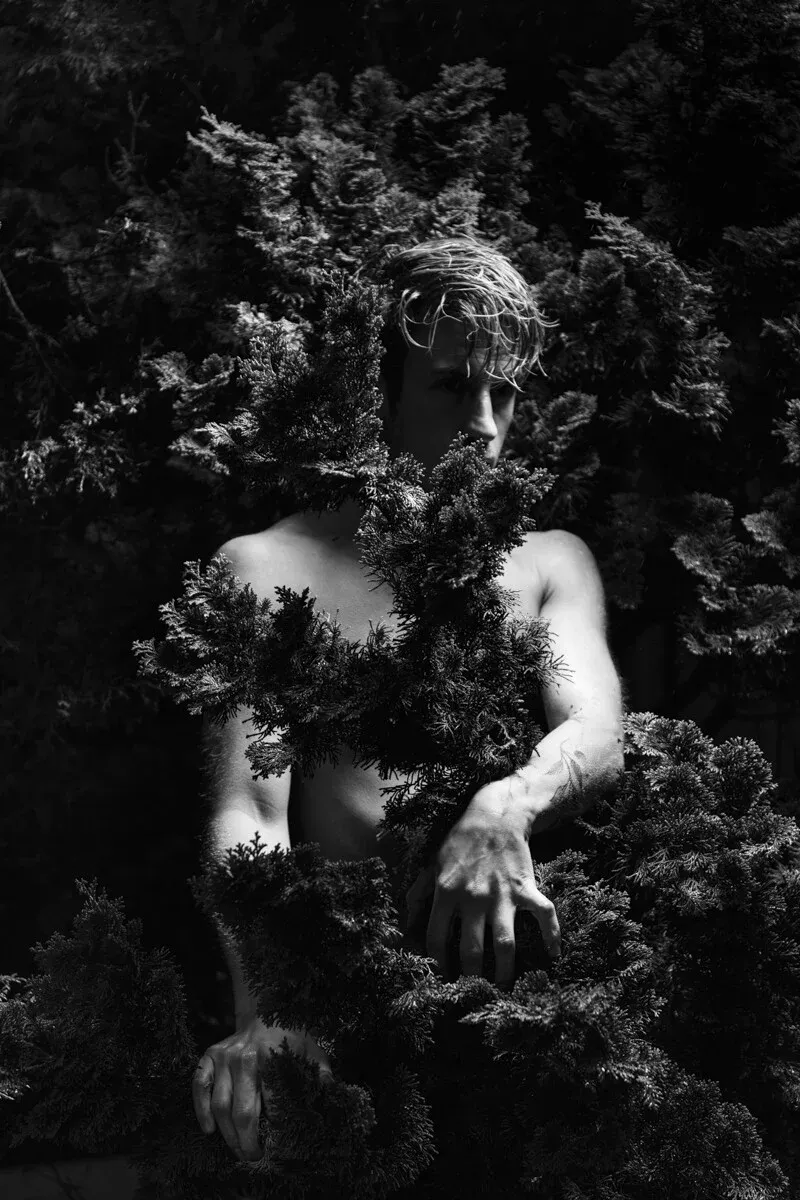 A high-contrast black and white conceptual portrait of STAN for the ESTRANGED series by ARJAN SPANNENBURG, featuring a man looking through dense foliage.