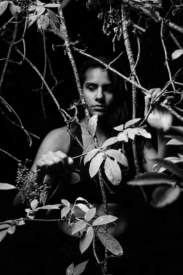 A black and white conceptual fine art portrait of SURAINA for the ESTRANGED series by ARJAN SPANNENBURG, featuring a woman looking through elderberry branches.