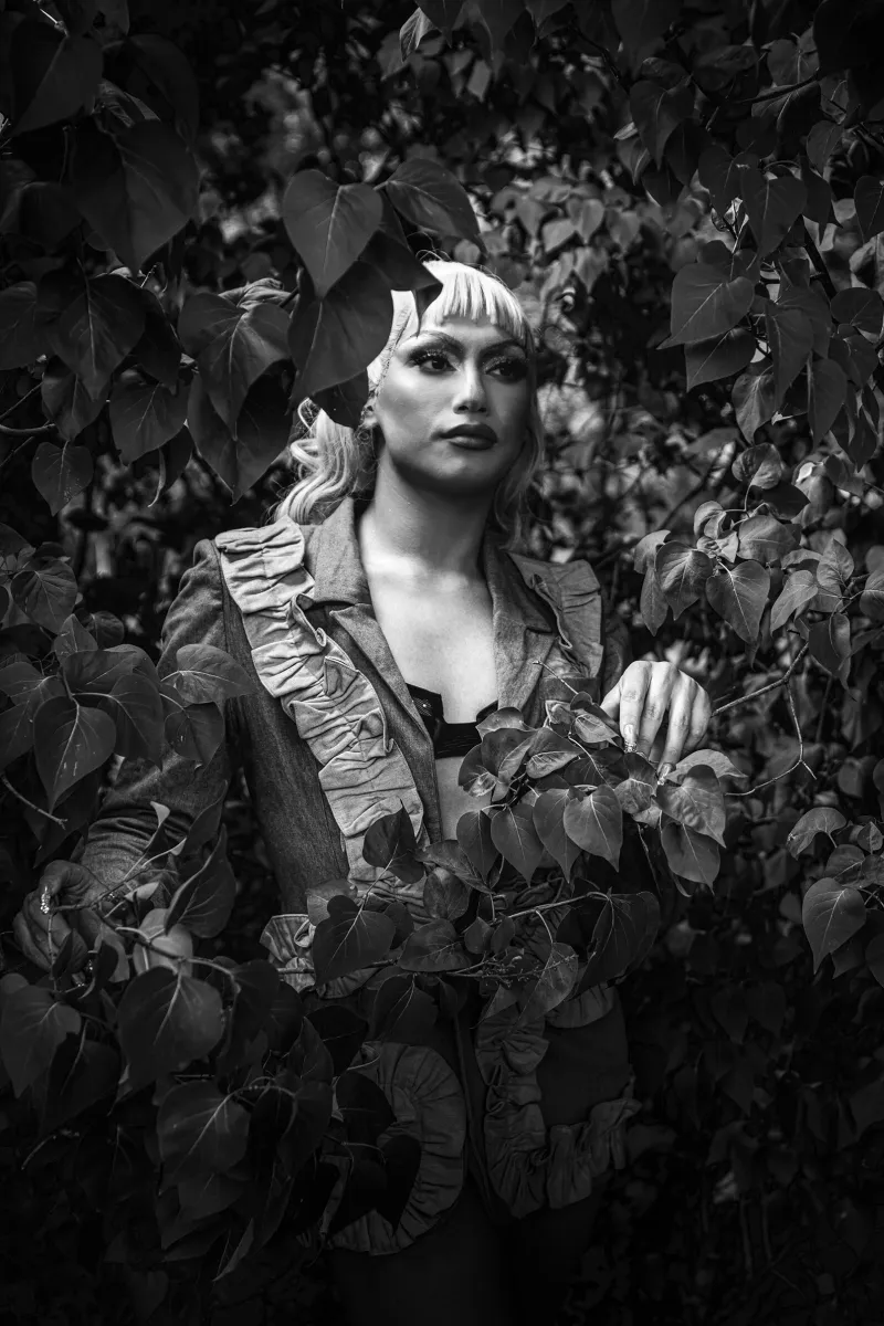 A black and white conceptual fine art portrait of TOOTSI for the ESTRANGED series by ARJAN SPANNENBURG, featuring a person in drag among large leaves.