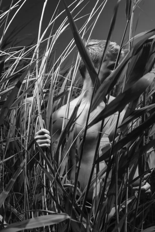 A black and white conceptual fine art portrait of ZICO for the ESTRANGED series by ARJAN SPANNENBURG, featuring a man among tall marsh reeds.
