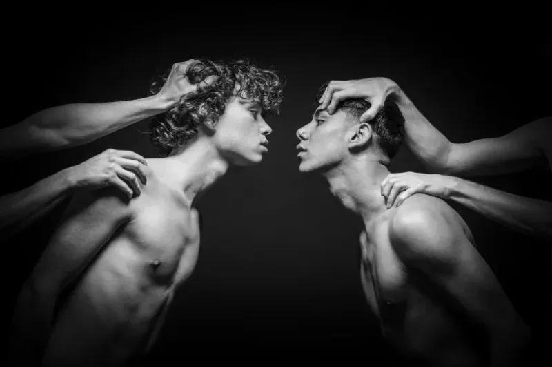 Restraint II by Arjan Spannenburg, a black and white photo of two men leaning together while being restrained by hands.